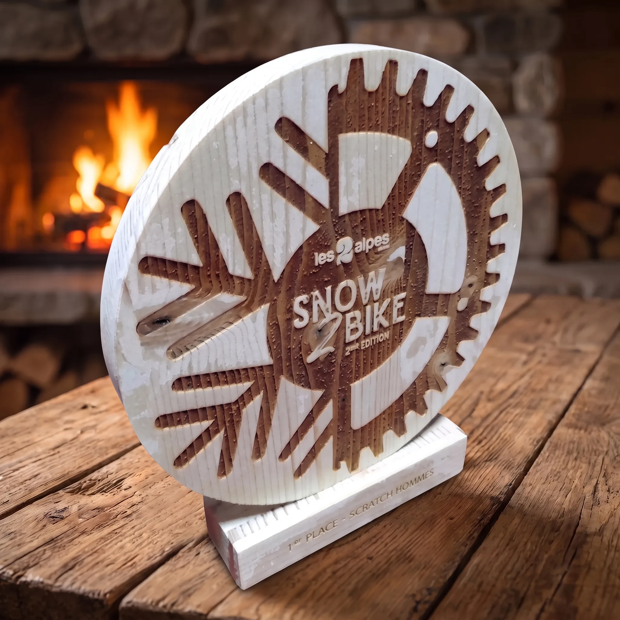 Trophée en bois rond personnalisé Snow Bike Les 2 Alpes, gravé au laser, 1ère place scratch hommes, posé devant une cheminée